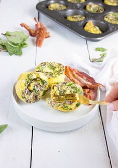 someone is holding a fork over some bacon and egg muffins on a white plate