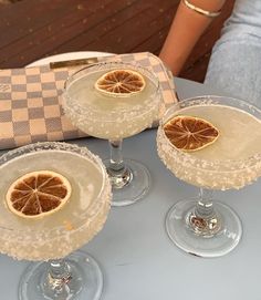 three wine glasses with orange slices in them sitting on a table next to a purse