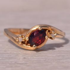 This Stunning Piece, Known As The Garnet Whisper, Features A Captivating Oval Cut Natural Garnet At Its Center. The Garnet Is Elegantly Flanked By Two Round Brilliant Cut Natural Diamonds, Adding A Touch Of Sparkle And Sophistication. The Ring Is Crafted In 14 Karat Yellow Gold And Is Currently A Finger Size 6.5 Yet Can Be Adjusted To Any Finger Size For An Additional Charge Upon Request, Ensuring A Perfect Fit. The Ring Bears A Designer Hallmark, Yet We Have Not Quite Identified The Maker Yet. Heirloom Red Jewelry With Diamond Accents, Fine Jewelry Garnet Rings Hallmarked, Unique Oval Garnet Rings, Oval Garnet Ring Hallmarked, Classic Yellow Gold Garnet Rings, Gold Garnet Rings With Cabochon, Ring Bear, Garnet And Diamond Ring, Garnet Engagement Ring