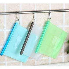 three clear bags hanging on a metal bar next to a green plant and white tiled wall