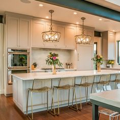 a large kitchen with white cabinets and wooden flooring, along with an island that has four bar stools in front of it