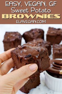 a hand holding a piece of brownie with chocolate frosting on top and other desserts in the background