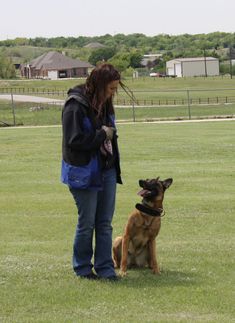 a woman standing next to a dog on top of a lush green field