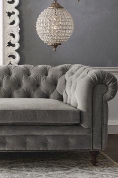 a gray couch in a living room with chandelier hanging from the ceiling and rug on the floor