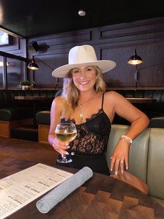 a woman sitting at a table with a glass of wine in her hand and menu on the table