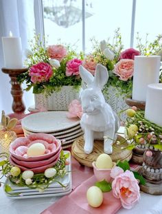 a table topped with plates and vases filled with flowers next to a bunny figurine