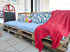 a couch made out of wooden pallets with a blanket over it and pillows on top