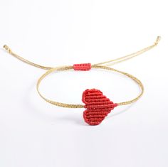 two red hearts are attached to a gold string bracelet with thread and beads on it