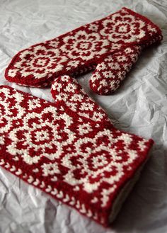 two red and white knitted mitts laying on top of a bed next to each other