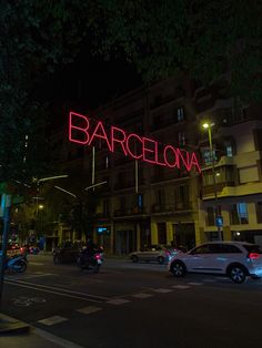 cars are parked on the street in front of a large neon sign that reads barcelona