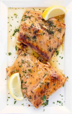 grilled salmon on a white plate with lemon wedges and parsley garnish