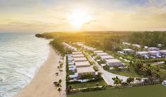 an aerial view of a beachfront resort with the sun setting over the ocean and houses