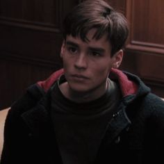 a young man sitting in front of a wooden paneled wall looking at the camera