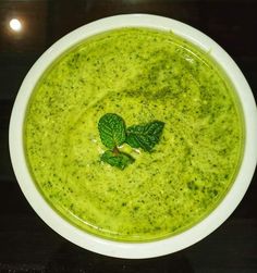 a white bowl filled with broccoli soup and garnished with green leaves