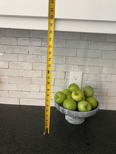 a bowl filled with green apples next to a measuring tape on top of a counter