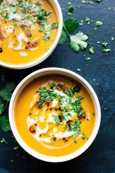 two white bowls filled with carrot soup and garnished with parsley