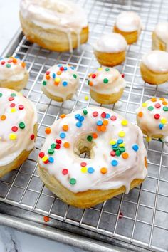 a bunch of doughnuts that are on a cooling rack in a kitchen with white frosting and sprinkles