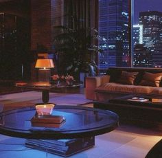 a living room filled with furniture and tall buildings in the background at night, lit up by candles