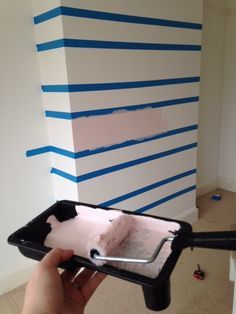 a person holding a paint roller in front of a wall with blue strips on it