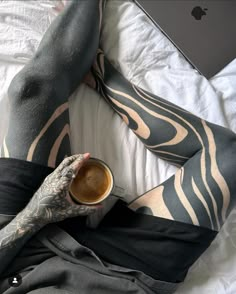 a person laying on top of a bed with their legs crossed holding a cup of coffee