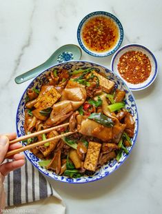 a person holding chopsticks over a bowl of food with meat and vegetables on it