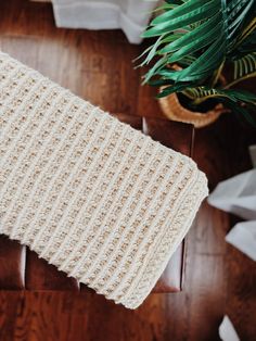 a white knitted blanket sitting on top of a wooden table next to a potted plant