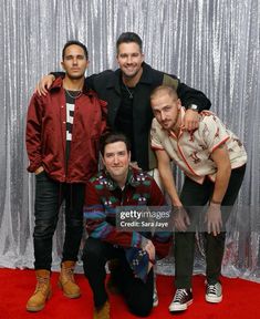 three men posing for the camera in front of a silver curtain and red carpeted backdrop