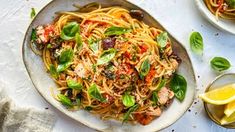 a plate of pasta with meat and vegetables on it next to two plates of lemon wedges