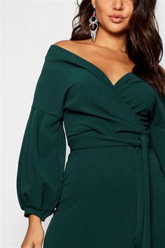 a woman wearing a green dress with an off the shoulder neckline and long sleeves