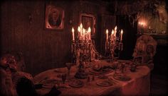 an old fashioned dining room with candles on the table and creepy looking chairs around it