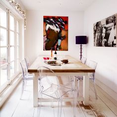 a dining room table with clear chairs in front of a large painting on the wall