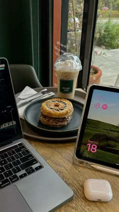 an open laptop computer sitting on top of a wooden table next to a plate with food