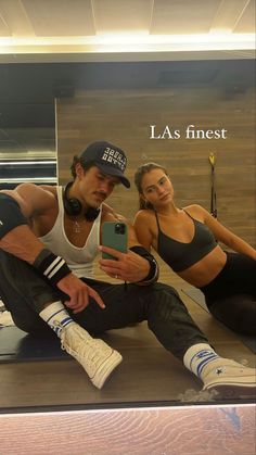 a man and woman sitting on the ground in front of a mirror taking a selfie