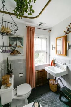 a white toilet sitting next to a sink in a bathroom under a window with orange curtains