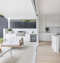 an open kitchen and living room area with white furniture, wood flooring and large sliding glass doors