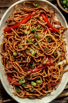 a white bowl filled with noodles and vegetables on top of a wooden table next to chopsticks