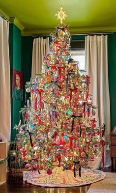 a brightly colored christmas tree in the corner of a room with green walls and curtains