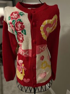 a red cardigan sweater with flowers and hearts on the front is hanging from a rack