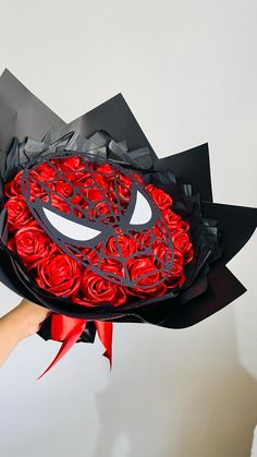 a person holding a bouquet of red roses in the shape of a spiderman mask