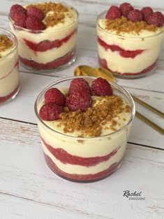 four desserts with raspberries and crumbs in small glass dishes on a white wooden table