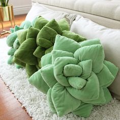 two green flower pillows sitting on top of a white rug in front of a couch