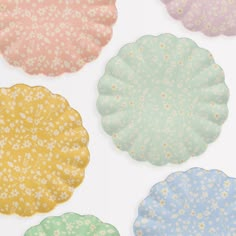 four different colored paper plates sitting on top of a white tablecloth covered in small flowers