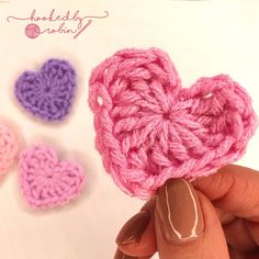 crocheted heart shaped object being held in front of three smaller hearts on white background