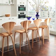 four chairs are lined up in front of a counter with a vase and flowers on it