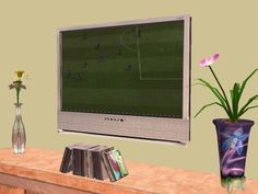 a computer monitor sitting on top of a wooden table next to a vase with flowers