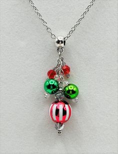 three christmas ornaments hanging from a silver chain on a white surface with red, green and black beads