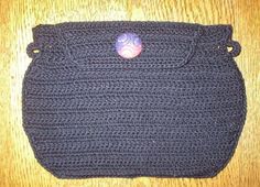 a crocheted purse with a button on the side sitting on a wooden table