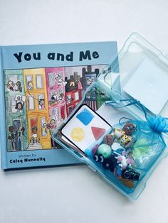 an open book and some toys in a plastic container on a table with a blue ribbon