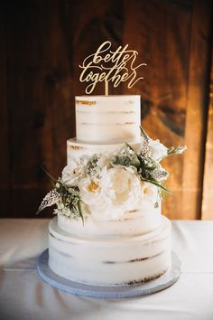 a three tiered cake with white flowers and gold lettering that says happy birthday on top