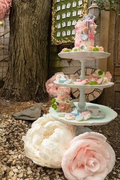 three tiered cake stand with pink and white flowers on the ground next to a tree